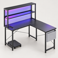 Bureau d'angle gaming en L 148 cm noir avec LED RGB et étagère, vue de trois quarts sur fond gris clair