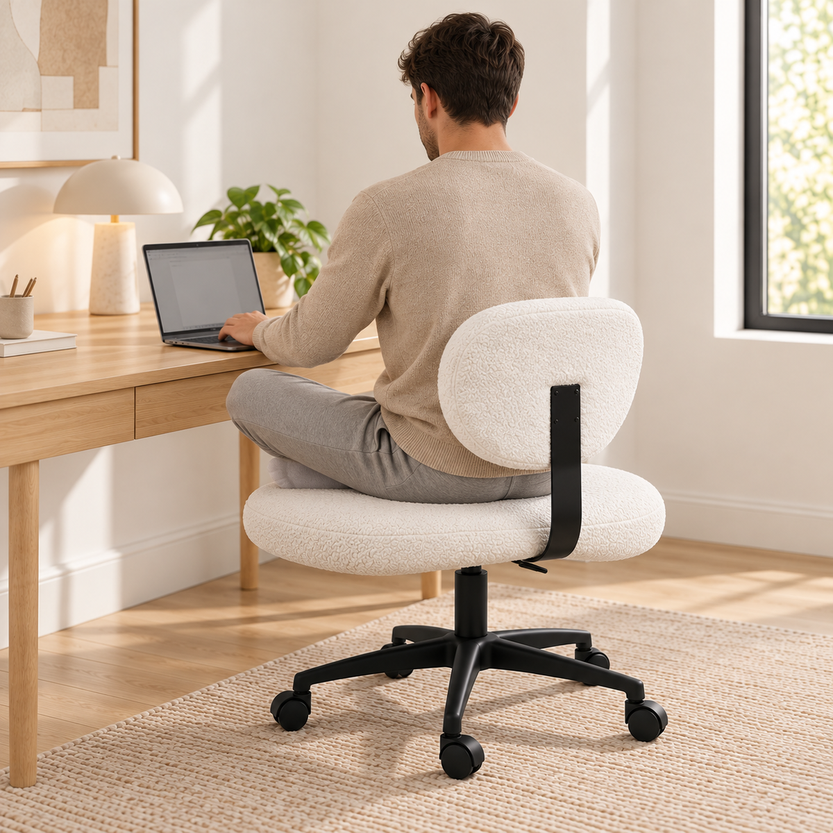 Homme assis en tailleur sur la chaise blanche, travaillant sur un ordinateur portable