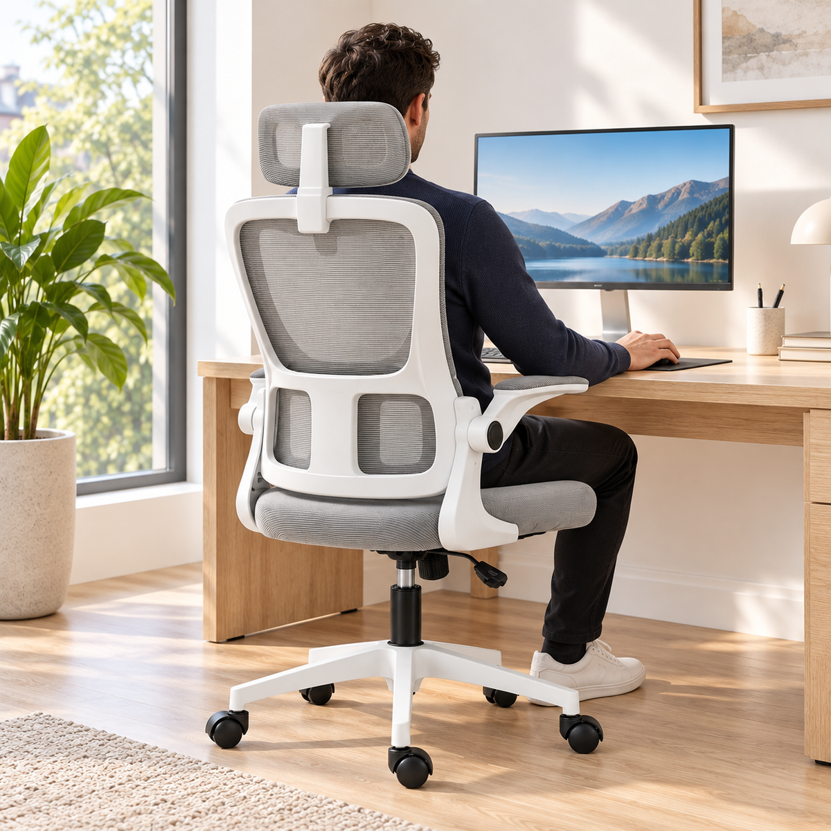 Homme assis dans le fauteuil de bureau en maille devant un écran, vu de dos